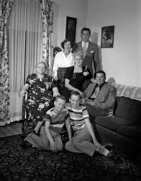 Portrait of the Herman Fischer family. Emmy Lou, 16, and Herman, Jr., 20, are standing in the back row.  Seated in the second row are Grandma Emma Fischer, 81, mother Ora Fischer and father Herman O.  'Hank' Fischer. In the front row Billy, 11, and Bobby, 13, smile from the floor. The Fischer family owned and operated a 10-acre farm and a roadside produce stand across the street (Monona Drive) from Monona golf course.