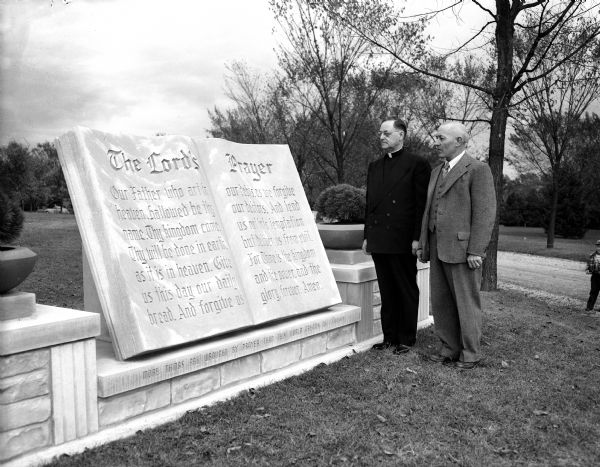 The Reverend Benjamin W. Saunders (left), Episcopal director of the DeKoven foundation of Racine, stands beside a marble marker monument inscribed with the Lord's Prayer at Roselawn Memorial Park, 119-122 Monona Drive. Stefan Mittler, Mittler Monuments, 29 North Orchard Street, sculpted the monument and Rev. Saunders dedicated the sculpture at dedication ceremonies. An unidentified man stands at right.