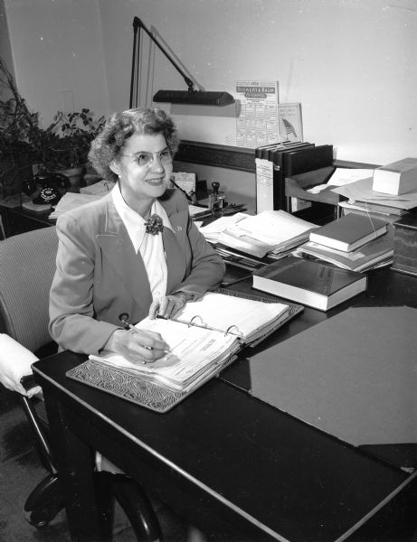 Mrs. Minnie R. Whipple sits at a desk in her office as purchasing agent for the board of regents of the state normal schools. She has held many offices in the Madison Business and Professional Women's Club which is participating in the National Business Women's Week.