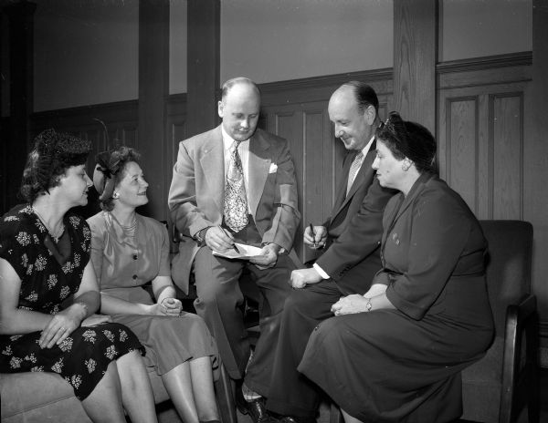 Two solicitors for the Madison United Givers' Fund drive of 1950, Mrs. Ellis (Helen) Wertz (left) and Mrs. Howard (Evelyn) Nedderman (second to left), listen to a discussion of the functions of the Associated Services for the Armed Forces (ASAF). The ASAF is one of the agencies taking part in the fund drive. Explaining the work of the ASAF to the solicitors are representatives of the three organizations making up the ASAF: left to right, Corwin Shell, YMCA; Edward J. Ownes, National Catholic Community Service; and Mrs. Morris (Belle) Richman, National Jewish Welfare Board.