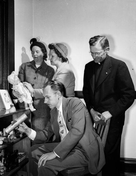 L.E. Rolefson, director of the Lutheran Welfare Society, seated, shows the Reverend E.J. Van Handel, director of the Catholic Welfare Bureau, and two United Givers' Fund solicitors, Mrs. Theo J. (Josephine) Scheerer, and Mrs. Lee J. (Florence) Favour, some of the toys which he keeps in his office to amuse the many youthful clients brought there. The Lutheran and Catholic Welfare groups, which deal principally in placing children in foster and adoptive homes, are among the agencies taking part in the 1950 United Givers' Fund drive.