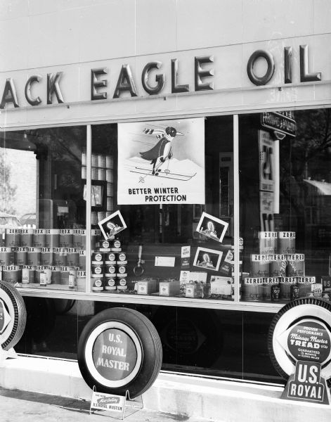 Close-up view of the show window at the Black Eagle Oil Company, 1039 East Washington Avenue, depicting a display of winter-weight oil and automobile tires.