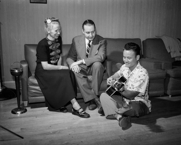 Dick Miyagawa, recreation director of the village of Shorewood Hills, is shown playing his Hawaiian guitar for Mr. and Mrs. Edwin (Elaine) Herbig at "Shindig," a Shorewood Community League fall event attended by approximately 250 Shorewood Hills residents.