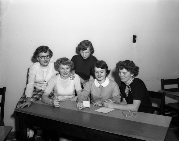 Five Rainbow Girls, committee chairmen for the "Scotch Fling" sweater and skirt dance, are seated around a table. Left to right are: LaVon Dailey, Donna Feggestad, Carma Rae Chapman, Donna Helleckson, and Karen Takle.