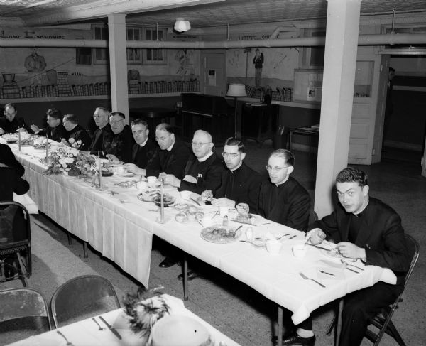 A group of priests sitting at the head table during the Blessed Martin Dinner at the St. Paul University Chapel, 717 State Street. Left to right: The Rev. George Hastrich, Milwaukee; the Rev. Christopher Fullman, Latrobe, Pennslyvania; the Revs. Alvin R. Kutchere, John Koelzer, and the Right Rev. Msgr. William H. Eggers, Madison; Father Jerome J. Hastrich, the Rev. Claude Heithaus, guest speaker, and the Right Rev. Msgr.George A. Haeusler, Sun Prairie; Rev. E.J. Graham, Sun Prairie; the Rev. E.J. Bauhs, Baraboo; and the Rev. Justinian Vereb, Hungary.