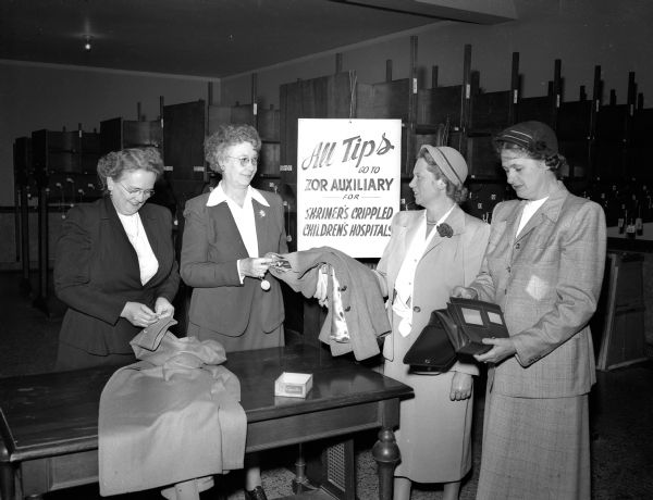 The Zor Shriner Auxiliary check room "concession" held at the Masonic Temple for all auxiliary social events is one of their many fund raising activities to benefit Shriners' hospitals for crippled children. Pictured are two members of the checking committee receiving tips from two other auxiliary members. Left to right: Mrs. George H. (Bessie) Russell, 103 North Seventh Street, and Mrs. Ethel Tuttle, 1 Langdon Street, both checkers, and Mrs. John M. (Viola) O"Neil, 314 North Blount Street, and Mrs. L.E. (Blanche) Hart, 4258 Manitou Way.