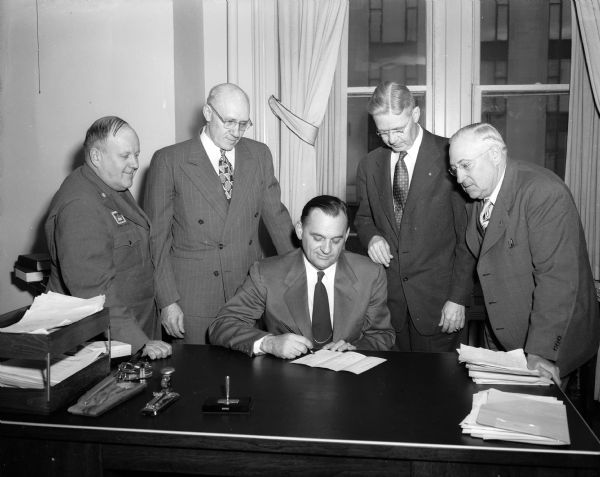 Acting City Manager George Forster signs a proclamation to observe Optimist Week in Madison. Standing left to right are: C. B. Beebe, director of the Optimist-sponsored Drum and Bugle Corps.; Ross Rowen, Director of the Junior Optimist oratorical contest; B. R. L'Hommedieu, president; and W. H. Moffit, chairman of Optimist Week.