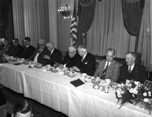 Ten men sitting at a table at the Madison Knights of Columbus 50th Anniversary Banquet at Hotel Loraine. Left to right: Anton L. Nussbaum, past grand knight and 45-year member; Judge Harold J. Lamboley, Monroe, state deputy; J. Vincent Conlin, grand Knight of the Madison council; Bishop William P. O'Connor, spiritual leader of the Madison diocese; Atty William Ryan, toastmaster; Dr. C.W. Henney, Portage, a supreme director; and the Rev. J.J. Mersberger, Immaculate Heart of Mary parish who gave the sermon at the mass held at St. Raphael's Cathedral.