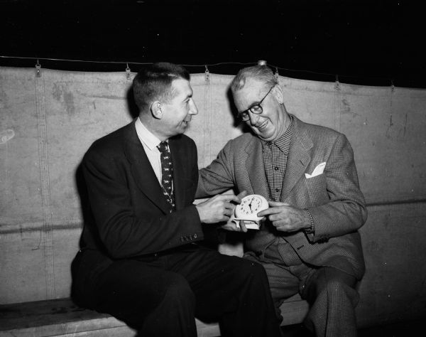 Journalist "Roundy" Coughlin (right) confers with Wisconsin basketball coach "Bud" Foster regarding an alarm clock.