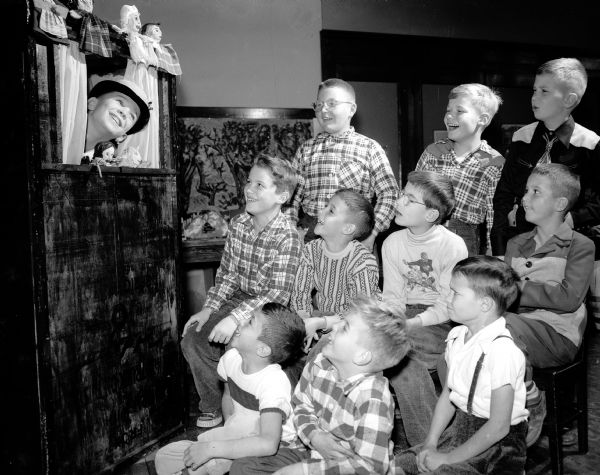 Nakoma School third grade children watching a class play, "Democracy for Boys and Girls." The children were assigned to find out where their ancestors came from and what they brought with them to America.  William Platz, representing Germany, is in the puppet box.
Watching are, left to right, first row, Frank Balisteri, representing Italy; Michael Jacobson, Czechoslovakia, and Steven Curtis, Ireland.  Second row: John Yount, Holland; Dale Conteht, Switzerland, Richard Gissendore, Germany; and Michael Lampman, Scotland.  Third row: Glenn Schoenenberger, Germany, and Neil Swanson, Norway.