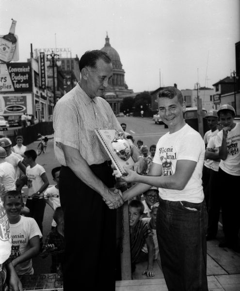 Don Knowles, general manager of Holt's Capital Garage and cosponsor of the race, presenting trophy to the winner Van Steiner. Buildings in the background are Pahl Tire Co., 209 East Washington Avenue on the right and Firestone Tires, 215 East Washington Avenue on the left, and the Wisconsin State Capitol in the center.