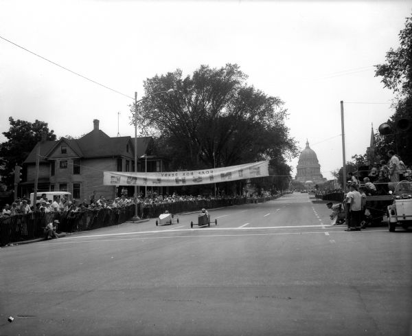 Finish line on East Washington Avenue of one of the heats at the 1957 Madison Soap Box Derby. The Wisconsin State Capitol is in the background.