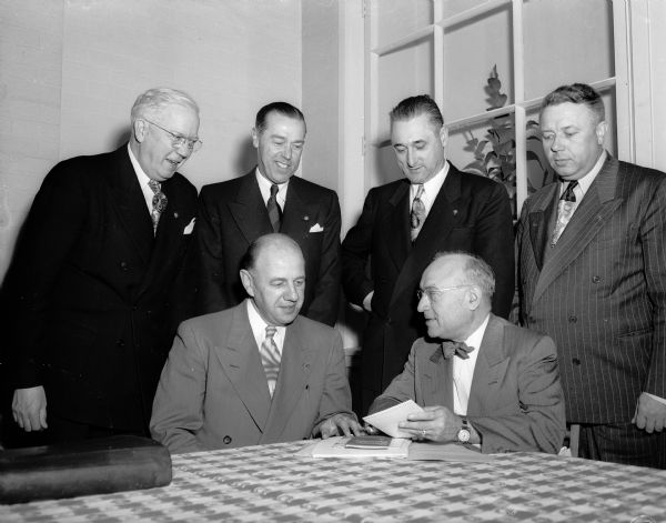 Officers of the Wisconsin-Upper Michigan district of Kiwanis International gather around a table during a two day training school in Madison. Left to right, seated:  Earl C. Knutson; Westby, district governor elect; and Frank J. Horak, Oconto, district governor.  Standing: Harrison U. Wood, Racine, chair of the committee on education; S.G. Johnson, Madison, National Convention chair; Frank Paitl, Marquette, Michigan, lieutenant-governor-elect and Glenn Harrison, Wausau, district secretary.