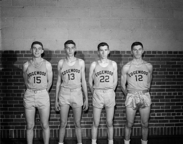 Four players of the Edgewood boy's basketball team, 1950-51 season, standing against a brick wall for a portrait. They are #15 LeRoy Berigan; #13 Bill Stam; #22 Ray Peteerson; and #12 Dick Kalscheur.