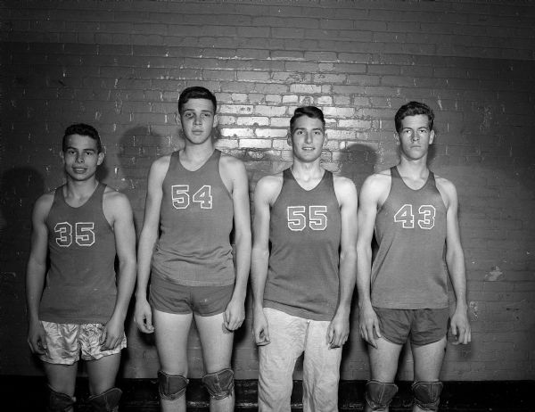 Four uniformed members of the Wisconsin High School basketball team posing for a group portrait. They are, from left to right: John Currie, Dennis Hawkes, Bruce Precourt, and (unknown).
