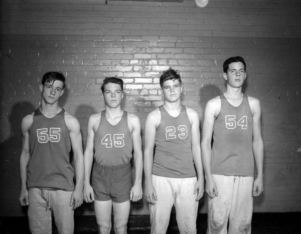 Four members of the Wisconsin High School basketball team posing in uniform for a group portrait. They are, from left:  Bruce Precourt, Jack Burkhalter (?), Richard Edwards (?), and Dennis Hawkes.
