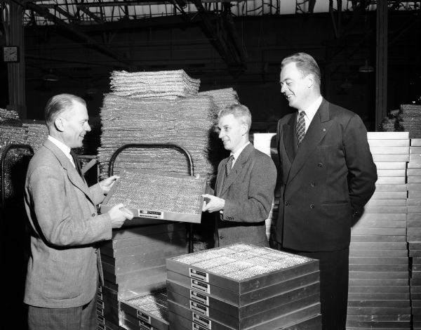 Three men look at the millionth filter produced by the Research Products Corporation, located at 1015 East Main Street. They are, from left to right:  R.E. Onstad, firm president; A.W. Brown, sales manager; and John G. Schultz, advertising manager.