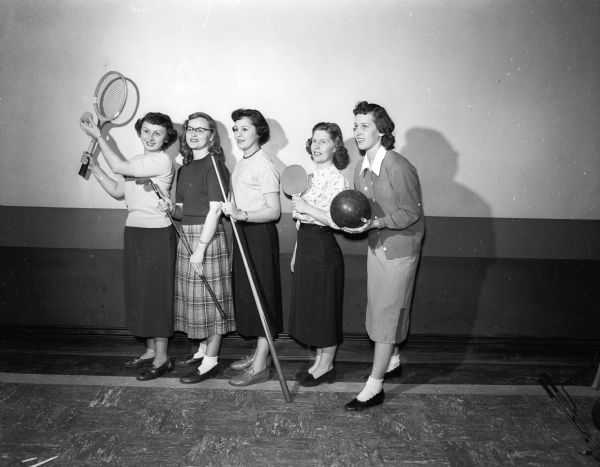 Five members of the Dames Club posing with sports equipment that depict activities the club will be involved in during the upcoming year. The Dames Club is a group for the wives of University of Wisconsin students. From left are Mrs. Fred Bencriscuito, Mrs. L.N. Van Dyke, Mrs. Ernie Nilo, Mrs. Elmo Earleywine, and Mrs. Ralph Jensen.