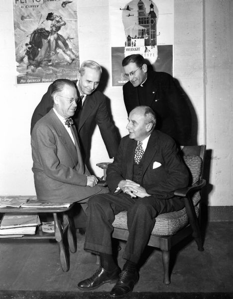 Red Cross officials gather at the annual meeting of the Dane County Red Cross chapter. Sitting left to right, they are: Herman Loftsgordon, Dane County Chairman, and Henry Tenny, Chicago member of the Board of Governors. Standing:  Rev. James R. Love, County Board of Directors, and Rev. E.J. Van Handel, Welfare Bureau of the Madison Catholic Diocese.