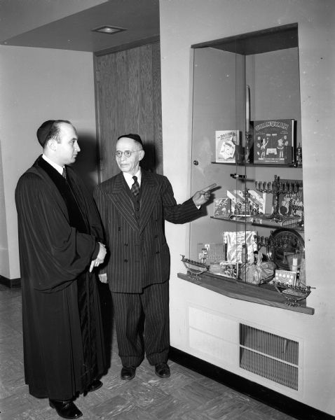 Rabbi Max A. Lipshitz (left) and sexton Abraham Gazevitz observe a display of books and symbols in the lobby of Beth Israel center that will be on display during the eight-day observance of Chanuka.