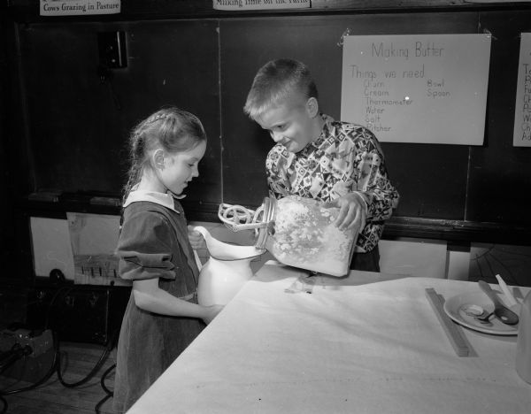 Second grade children of Lowell School engaging in a class project of making butter as part of a dairy study. Neil Nygaard (right) is pouring off the buttermilk, with Karen Natvig assisting.