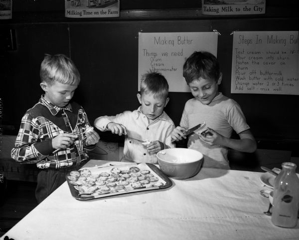 Second grade children of Lowell School engaging in a class project of making butter as part of a dairy study. Left to right, spreading butter on crackers, are John Olson, Tim Holt, and Ronald Peirce.