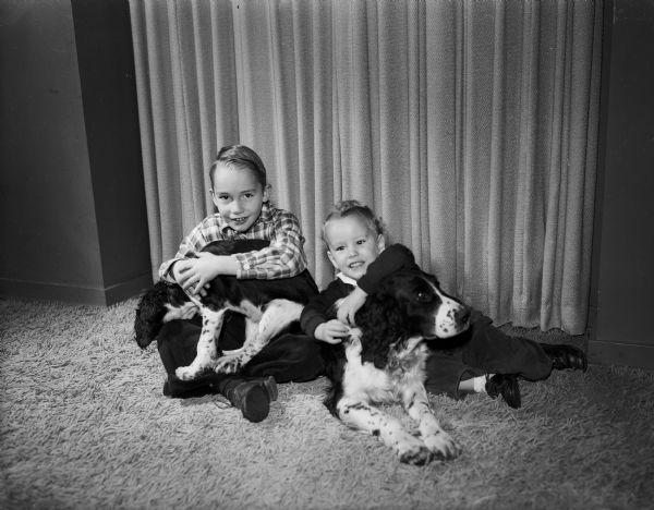 Brothers Billy Jasper, age 6, and Tommy Jasper, age 2, posing on shag carpeting with their Springer Spaniels, "Cissie" and "Mike."