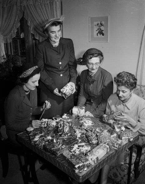 Members of the Who's New Club are shown wrapping some of the many presents they will distribute to the patients out at Mendota State Hospital (Mendota Mental Health Institute). They are, (L to R): Mrs. H.B. Saunders, Mrs. Grace Fakler, Mrs. J.J. Cole, and Mrs. Evelyn C. Jolliffe.
