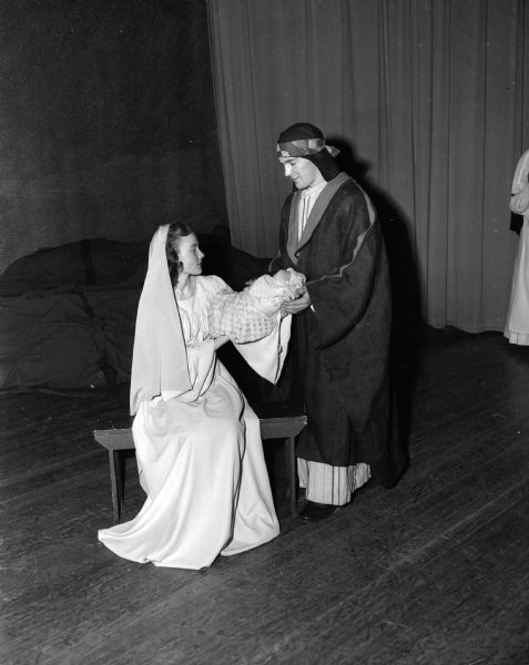 Two costumed actors standing and sitting on stage during the Christmas pageant presented by Edgewood High School seniors.  Marie Anthony and John McCormick were cast as the Virgin Mary and Joseph.