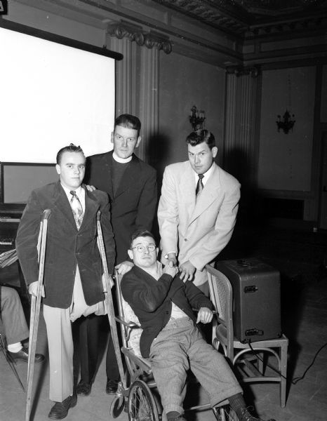 Shown from left to right are Vincent Peterson using crutches, the Reverend Jerome Mersberger, pastor of the Immaculate Heart of Mary Church, and Mickey Hall, seated in a wheelchair, shaking hands with Robin Roberts. Roberts was a baseball pitcher with the Philadelphia Phillies. He spoke to fans at the Loraine Hotel at a fund raiser sponsored by the Immaculate Heart of Mary Church with all proceeds going towards the construction of a playground for the youngsters of Monona village and Blooming Grove township.