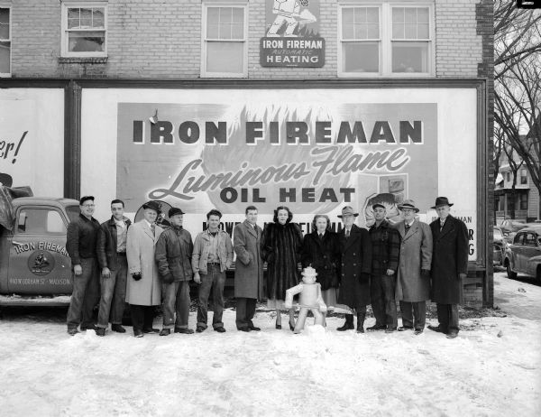 A group of men and women stand in front of the Midwest Iron Fireman Company at 440 West Gorham Street.