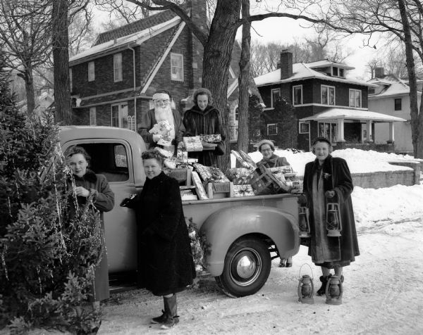 Members of the East Side Women's Club stand beside a truck full of Christmas presents for the patients at Lake View and Morningside sanatoriums.   They are, from left to right, Mrs. Robert (Evelyn) Fletcher, Mrs. H.W. (Marvel) Risberg, Santa Claus in the form of Mrs. Edward (Lois) Brandes, Mrs. George (Delores) Peck, Mrs. Norman (Jean) Scovill and Mrs Arthur W. Swan.  The truck is parked in front of 2734 & 2738 Lakeland Avenue.