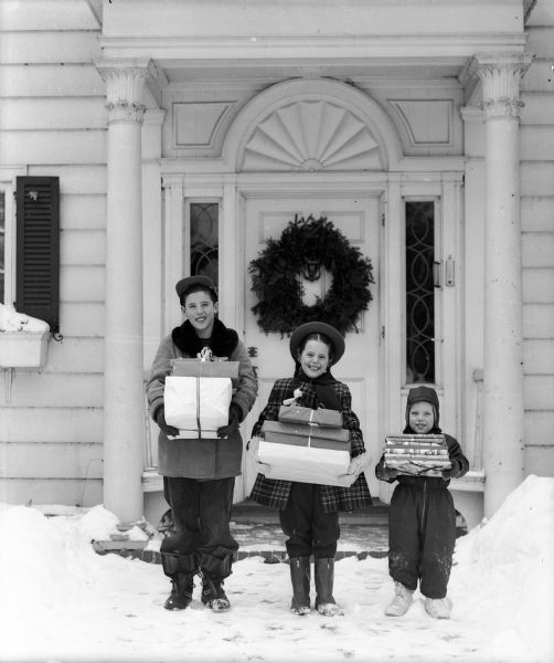 Jeffery, age 10, Leslie, 6, and Kurt, 3, children of Dr. Leslie and Jean Antonius, hold wrapped Christmas gifts while standing in front of their home at 325 Lakewood Boulevard, Maple Bluff.