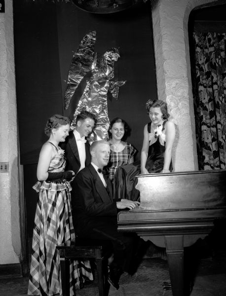 Robert Edmondson, featured entertainer at the University Club Christmas Dance, sits at a piano while surrounded by (left to right) Karen Ragatz, Ted Martin, Ann Seibold and Virginia Hammen.