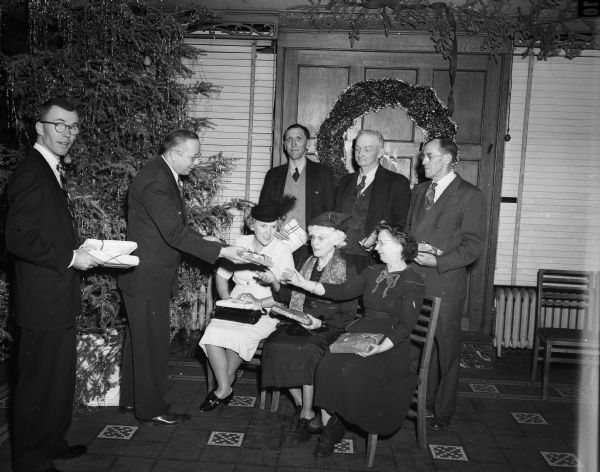 Six residents of the Verona Home for the Aged attend the annual Christmas party sponsored by the Madison Association of Underwriters at the Park Hotel. John Zimdars, left, Underwriters treasurer, and Don Hanesworth, right, president, are shown presenting gifts to (seated left to right) Mrs. Mina Cramer, Mrs. Cova Whitcomb, Minerva Holland, and (standing left to right) Oscar Strander, Paul Mahoney, and Carl Frydenlund.