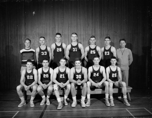 Group portrait of the East High School Basketball team in uniform with their coach and manager.  Left to right: Ted Blackney, Keith Brockmill, Jim Kurth, Gary Messner, Lloyd Sarbacker, Davey Johnson, and Ronnie Scharg. Back row: Manager Dick Skolen, Gordy Morris, Charles Brendler, Lee Schlicht, Clair Oren, Dean Sapith and Coach Milt Diehl.