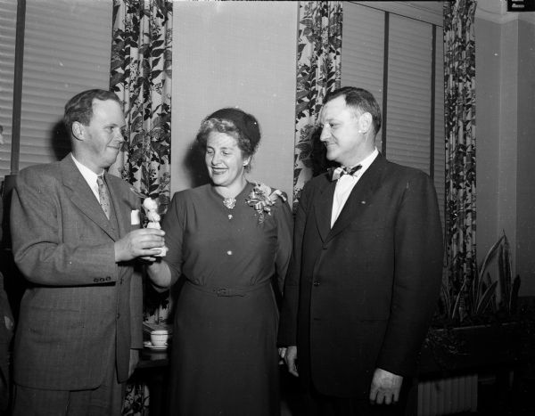 Mrs. Harriet Mead Haas is presented with a doll called "Red Feather Kid" and silver pin for her services to the Madison Community Chest. At left is Francis F. Bowerman, Jr. president of the Community Chest. Looking on is Bernhard Mautz, president of the United Givers' Fund.