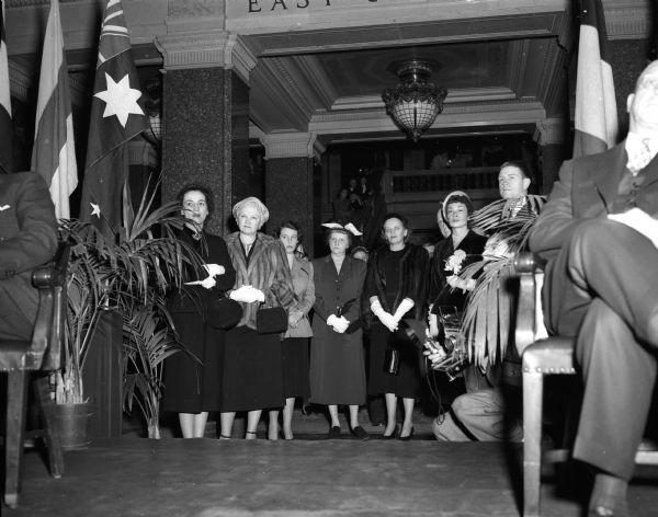 Women standing while watching Walter J. Kohler Jr.'s inauguration from the East Wing of the Capitol Building. They are, left to right: Mrs. Fred Gimbel, New York; Mrs. Mary Rennebohm; her daughter Carol Rennebohm; Mrs. Rosa P. Fred, wife of the UW President; Mrs. Earl Johnson, Washington D.C., wife of the assistant secretary of the army; and Mrs. Charlotte Kohler, wife of the governor-elect.