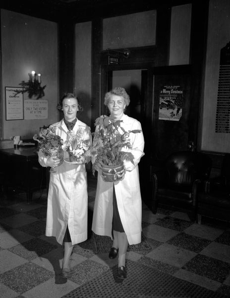 Madison General Hospital Auxiliary volunteer workers, Dorothy (Robert W.) Wylde, left, and Margaret (Eldon B.) Russell, deliver plants to hospital patients.