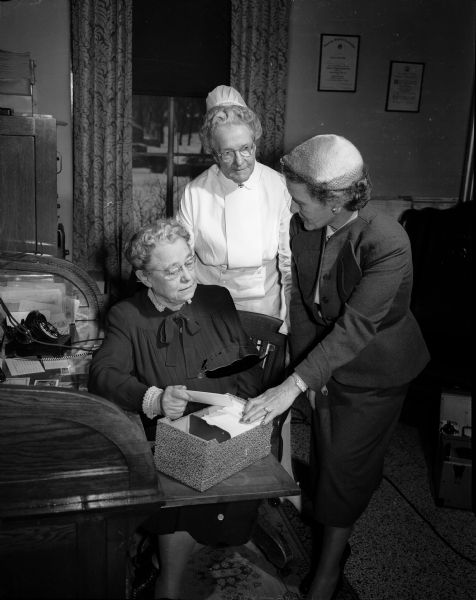 Catherine Coleman, standing right, chair of the Madison General Hospital Auxiliary Memorial Fund, showing her card file to Grace Crafts, hospital administrator, sitting, and Ida Collings, director of nursing at the hospital.