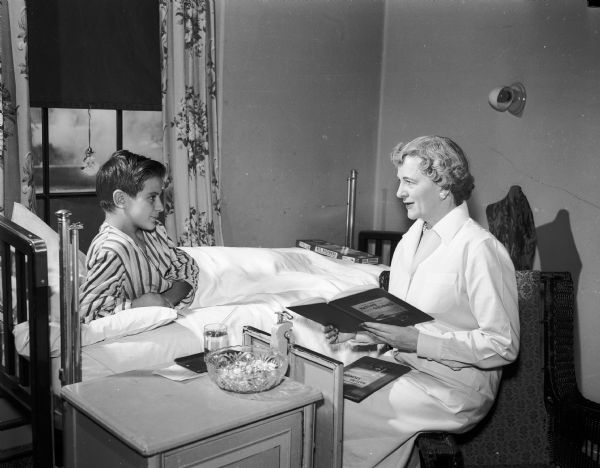 Madison General Hospital Auxiliary volunteer worker Mabel Lewis reading to Billy McCord, patient.