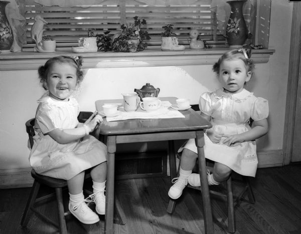 Pamela and Penelope, twin 3-year-old daughters of Mr. and Mrs. Manley R. Showers, sitting at a table while playing with a tea set.