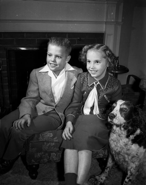 John and Mary Pavlak, 9-year-old twins of Mr. and Mrs. Ray Pavlak, posing near a fireplace with their dog, Queenie.
