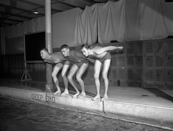 Bob Feirn of Madison (left), Alvo Cherne of Milwaukee (center), and Jerry Smith of Kenosha, members of the University of Wisconsin Men's Swim Team who rated an All-American mention in the previous year, pose at the deep end of an indoor swimming pool.