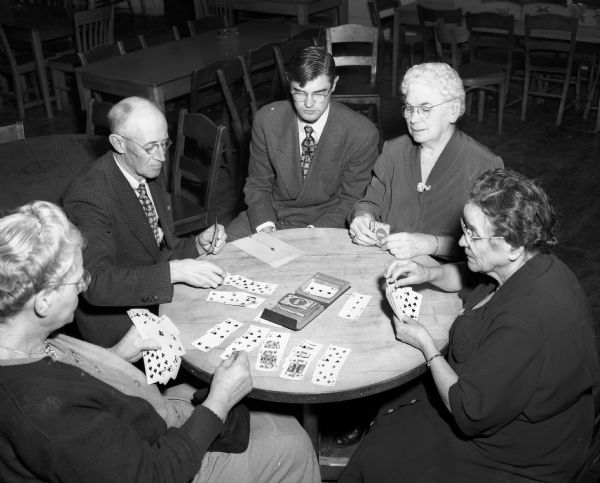 A group of retired people play a game of canasta at the Social Afternoon Klub which is held weekly at the Madison Community Center. The Social Afternoon Klub is a new club recently organized through the efforts of a UW Sociology Department student project for Madison's growing population of over-age-65 retired people. Pictured left to right are: Sarah Brockmiller; Fred J. Courture; UW student Harold Schrage, one of the club organizers; Mrs. M. Riemer; and Alma Price.