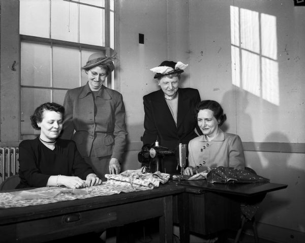 Four members of the University League make aprons for the homecrafters to wear while they do their craft work for the state rehabilitation center at Truax Field. They are, left to right: Mrs. Lorentz H. (Mildred) Adolfson, Mrs. Ira L. (Mary) Baldwin, Mrs. Edwin B. (Rosa) Fred, and Mrs. Henry L. (Harriet) Ahlgren.