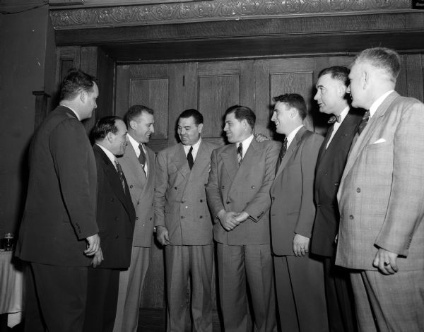 The members of the U.W. football coaching staff are shown meeting with Jack Dempsey, former world's heavyweight boxing champion during a dinner at the Park Hotel. Dempsey was in Madison to referee the windup bout of Promoter Jimmy Demetral's weekly wrestling show at the Eagles Club. Shown left to right are: Paul Shaw, end coach; Demetral; Ivan "Red" Williamson, head coach; Dempsey; Milt Bruhn, line coach; Bob Odell, backfield coach; George Lanphear, freshman coach, and Fred Marsh, junior varsity coach and chief scout.