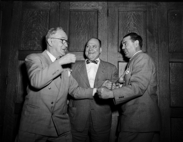 Three smiling men are posing in a pretend boxing stance at the Park Hotel. On the right is former world heavy weight boxing champion, Jack Dempsey. On the left is "Roundy" Coughlin (?). In the middle, playing referee, is wrestling promoter Jimmy Demetral (?).