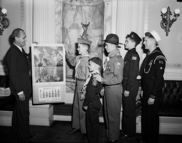Five Madison Boy Scouts present the 1951 Boy Scout calendar to Governor Walter Kohler.  Included in the photograph, from left, are: Governor Kohler; Air Scout Dick Merkel; Cub Scout Douglas Backus; Boy Scout Charles Johnson; Explorer Scout Richard Willis; and Sea Scout Fritz Turner.