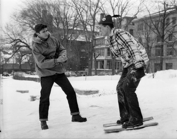 An unidentified University of Wisconsin student looks on as fellow student, Jim Healy of Milwaukee (right), practices for the barrel stave races. The race is one of the Wisconsin Hoofers Winter Carnival activities.